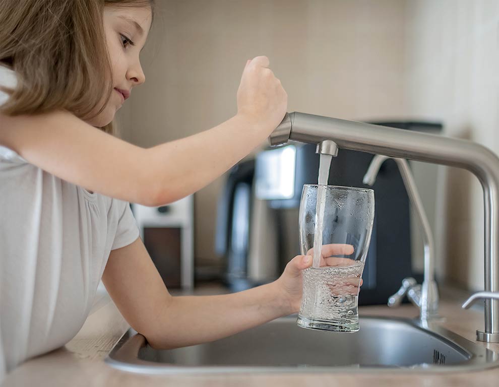 Ein Kind schenkt sich ein Glas Wasser ein als Zeichen für sauberes Trinkwasser 